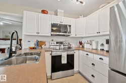 Kitchen featuring white cabinetry with black hardware, stainless steel appliances, laminate countertops, and a stainless steel sink with a black faucet - 