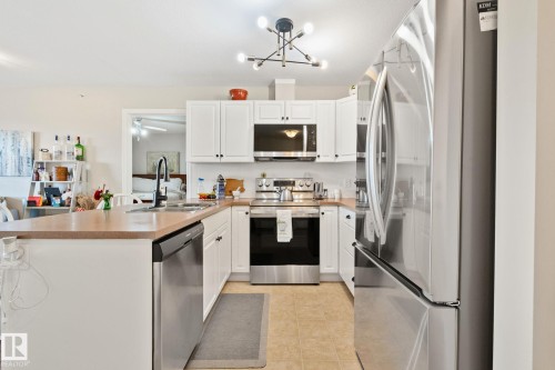 White cabinetry with black hardware, stainless steel appliances, a center island with sink, and a contemporary light fixture - #407 4309 33 St, Stony Plain, AB - Indoor Photo Showing Kitchen