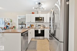 White cabinetry with black hardware, stainless steel appliances, a center island with sink, and a contemporary light fixture - 