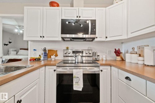 White cabinetry with dark hardware, stainless steel appliances, light-toned countertops, and a white tile backsplash - #407 4309 33 St, Stony Plain, AB - Indoor Photo Showing Kitchen