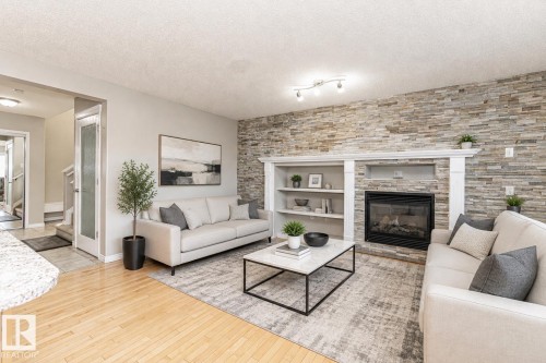 Staged with AI - Living area featuring wood-finish flooring, a stacked stone accent wall, a built-in fireplace with a white mantel, and integrated shelving - 192 Keyport Circle, Leduc, AB - Indoor Photo Showing Living Room With Fireplace