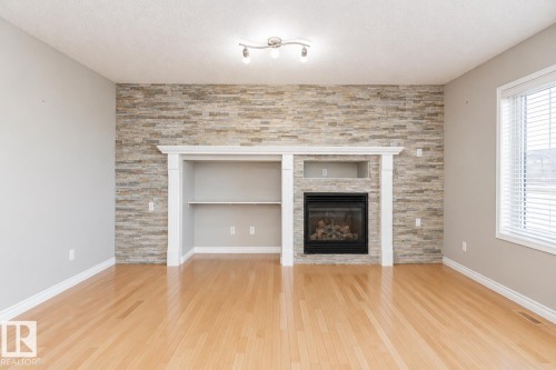 Stone accent wall featuring a built-in fireplace and integrated shelving - 192 Keyport Circle, Leduc, AB - Indoor Photo Showing Living Room With Fireplace