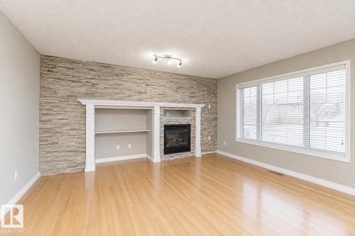 Hardwood-finish flooring, a stacked stone accent wall, built-in shelving, an integrated fireplace, and a large multi-pane window - 192 Keyport Circle, Leduc, AB - Indoor Photo Showing Living Room With Fireplace