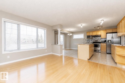 Hardwood-finish flooring, large window with blinds, kitchen island with built-in sink, stainless steel appliances, and wood-finish cabinetry - 192 Keyport Circle, Leduc, AB - Indoor Photo Showing Kitchen