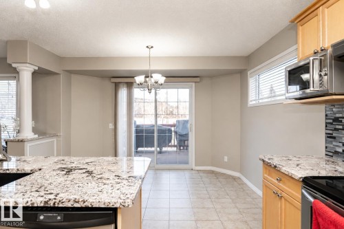 Kitchen with granite countertops, tile flooring, light wood cabinetry, and a sliding glass door to an outdoor patio - 192 Keyport Circle, Leduc, AB - Indoor Photo Showing Kitchen With Upgraded Kitchen