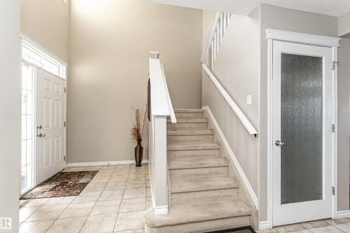 Foyer featuring a grand two-story ceiling, light-toned tile flooring, a white paneled entry door with decorative glass, a carpeted staircase with white railings, and a white interior door with frosted glass - 192 Keyport Circle, Leduc, AB - Indoor Photo Showing Other Room
