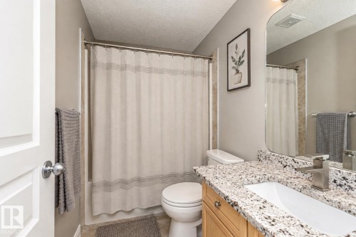 Bathroom featuring a combination bathtub and shower, a light wood-finish vanity with a granite-style countertop, an undermount sink, and a framed mirror - 192 Keyport Circle, Leduc, AB - Indoor Photo Showing Bathroom