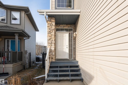 Exterior entrance featuring a white panel door with transom window, stone veneer accents, and light-toned siding - 192 Keyport Circle, Leduc, AB - Outdoor With Exterior
