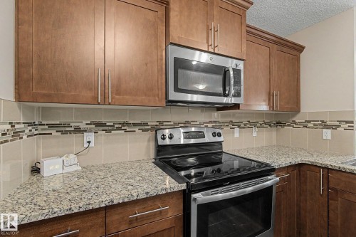 Kitchen featuring granite countertops, wood cabinetry, stainless steel microwave, and a black electric range with a stainless steel accent - 17304 73 Street Nw, Edmonton, AB - Indoor Photo Showing Kitchen