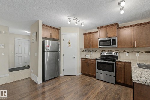 Modern kitchen featuring wood-finish flooring, stainless steel appliances, granite countertops, and rich wood cabinetry - 17304 73 Street Nw, Edmonton, AB - Indoor Photo Showing Kitchen With Stainless Steel Kitchen