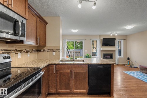 Open-concept kitchen featuring wood-finish cabinetry, stainless steel appliances, granite-style countertops, and a tile backsplash - 17304 73 Street Nw, Edmonton, AB - Indoor Photo Showing Kitchen With Fireplace