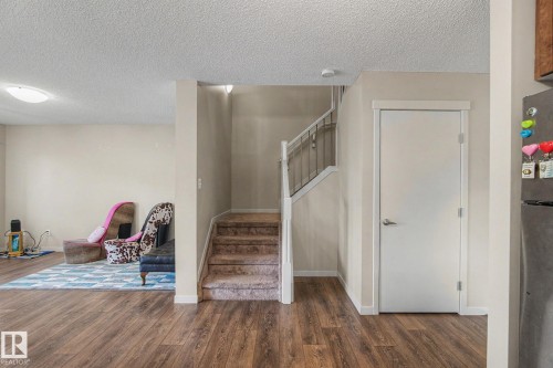Open-concept living space featuring wood-finish flooring, neutral wall tones, and a carpeted staircase with white railing - 17304 73 Street Nw, Edmonton, AB - Indoor Photo Showing Other Room