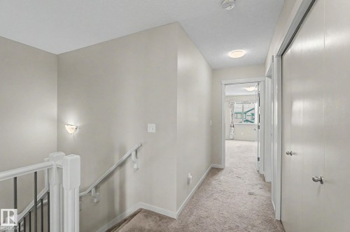Carpeted hallway with light neutral wall paint and white trim, featuring a flush mount ceiling light, a wall sconce, and two white bi-fold closet doors - 17304 73 Street Nw, Edmonton, AB - Indoor Photo Showing Other Room