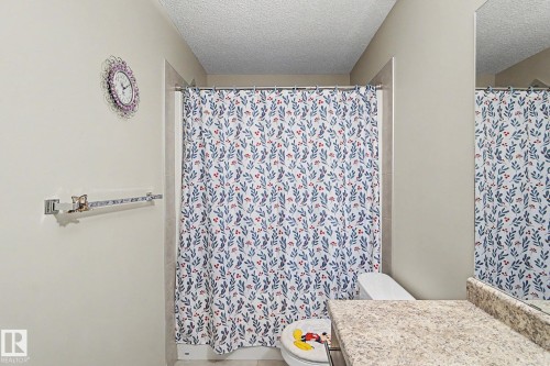 Bathroom with light-toned walls, a shower featuring a full-height shower curtain, a white toilet, and a vanity with a speckled countertop and integrated sink - 17304 73 Street Nw, Edmonton, AB - Indoor