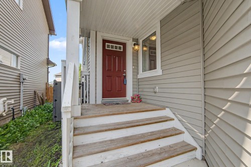Front entry featuring a red paneled door, wood porch steps, and light-colored siding - 17304 73 Street Nw, Edmonton, AB - Outdoor With Deck Patio Veranda