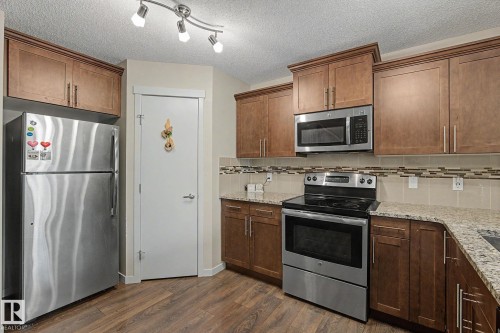 Kitchen featuring wood-finish flooring, stainless steel appliances, granite-style countertops, wood cabinetry, and a decorative tile backsplash - 17304 73 Street Nw, Edmonton, AB - Indoor Photo Showing Kitchen With Stainless Steel Kitchen
