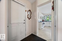 White paneled door with horizontal blinds, leading to a kitchen featuring white cabinetry, a large window, a white range, and light-toned flooring - 
