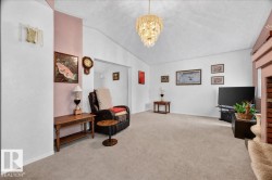 Vaulted ceiling featuring a decorative chandelier, neutral carpeting, and a brick fireplace surround - 