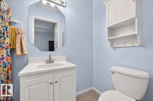 White vanity with integrated sink, brushed nickel faucet, octagonal mirror, wall-mounted storage cabinet, and porcelain toilet - 121 51205 Range Road 195, Rural Beaver County, AB - Indoor Photo Showing Bathroom