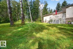 Expansive lawn with mature trees and a rear deck featuring lattice detailing - 