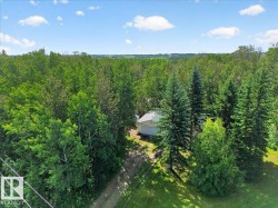 Wooded property with a single-story home featuring an attached garage and a gravel driveway - 