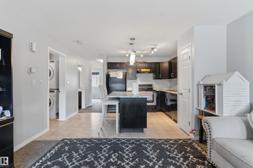 Kitchen with dark cabinetry, stone-finish countertops, stainless steel appliances, and an island with bar seating - #30 3305 Orchards Link Sw Sw, Edmonton, AB 