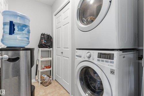Laundry area featuring a stackable washer and dryer, tile flooring, and a bifold door - #30 3305 Orchards Link Sw Sw, Edmonton, AB 