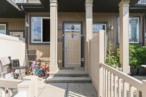 Entry featuring a beige paneled door, exterior wall sconces, and a window with white trim - #30 3305 Orchards Link Sw Sw, Edmonton, AB 