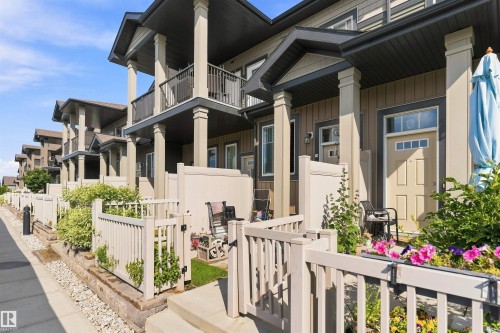 Multi-level townhome exterior featuring an upper balcony, covered entrance, and a ground-level patio enclosed by a privacy fence - #30 3305 Orchards Link Sw Sw, Edmonton, AB 