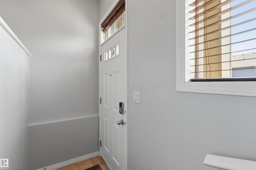 Entry with a white paneled door, transom windows, and an adjacent window with wood-finish blinds - #30 3305 Orchards Link Sw Sw, Edmonton, AB 