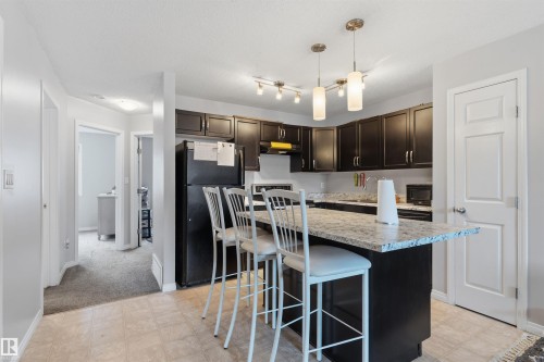 Kitchen featuring dark cabinetry, white-flecked countertop, stainless-steel sink, and track lighting with pendant fixtures - #30 3305 Orchards Link Sw Sw, Edmonton, AB 