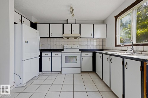 White appliances, tile flooring, window with exterior scenery, overhead lighting, and extensive cabinetry - 3515 43 Avenue Nw, Edmonton, AB - Indoor Photo Showing Kitchen