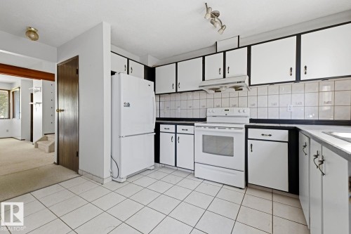 Kitchen featuring white tile flooring, white appliances, dark countertops, white upper cabinetry, and a tile backsplash - 3515 43 Avenue Nw, Edmonton, AB - Indoor Photo Showing Kitchen