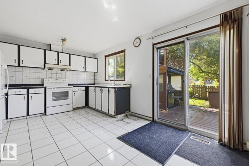 Kitchen with white tiled flooring, white cabinetry with black accents, white appliances, and a sliding glass door leading to an exterior deck - 3515 43 Avenue Nw, Edmonton, AB - Indoor Photo Showing Kitchen