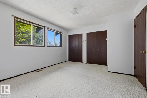 Light-colored carpeting, two windows with dark wood-finish frames, two sets of dark wood-finish bi-fold closet doors, and a single dark wood-finish door with a brass-finish doorknob - 3515 43 Avenue Nw, Edmonton, AB - Indoor Photo Showing Other Room