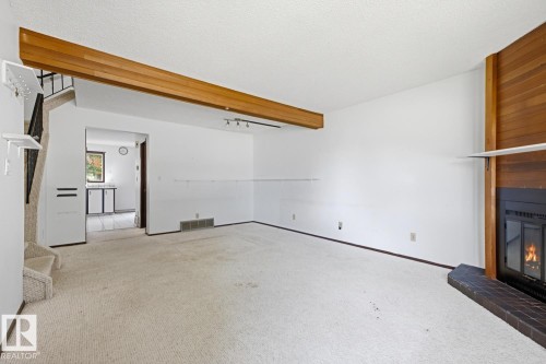 Living area featuring a floor-to-ceiling fireplace with a dark tile hearth, a wood-paneled accent wall, and a prominent exposed wood beam - 3515 43 Avenue Nw, Edmonton, AB - Indoor Photo Showing Other Room With Fireplace