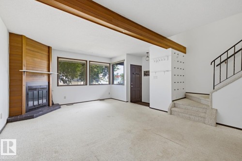 Living space featuring a wood-panel accent wall with a fireplace, multiple windows, a wood beam ceiling, and a carpeted staircase with a metal railing - 3515 43 Avenue Nw, Edmonton, AB - Indoor Photo Showing Other Room