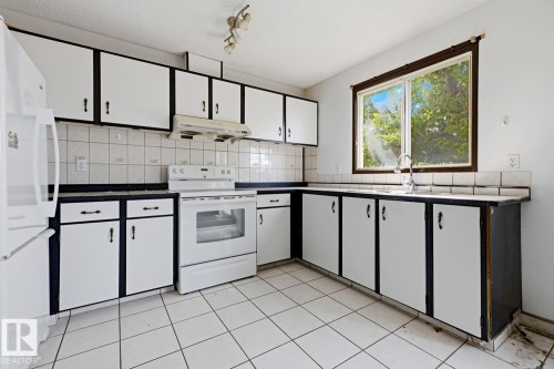Kitchen featuring white tile flooring, white cabinetry with dark trim, dark countertops, white tile backsplash, and a window - 3515 43 Avenue Nw, Edmonton, AB - Indoor Photo Showing Kitchen