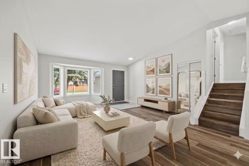 Wood-finish flooring throughout, featuring a bay window, a recessed ceiling light, and a built-in staircase - 4209 25 Avenue Nw, Edmonton, AB - Indoor Photo Showing Living Room