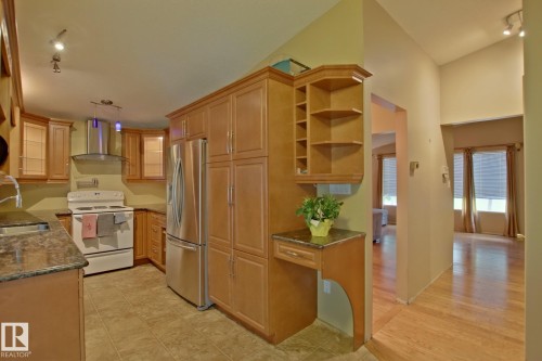 Kitchen featuring extensive wood-finish cabinetry, stainless steel refrigerator, white range, and stone countertops - 18107 89 Avenue Nw, Edmonton, AB - Indoor Photo Showing Kitchen