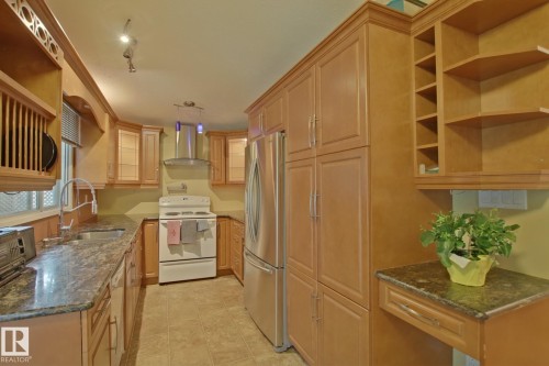 Full-height cabinetry, stainless steel refrigerator, stone-finish countertops, tile flooring, and a stainless steel range hood - 18107 89 Avenue Nw, Edmonton, AB - Indoor Photo Showing Kitchen
