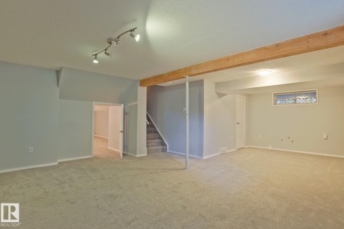 Expansive carpeted area featuring track lighting, a wood beam accent, and a window for natural light - 18107 89 Avenue Nw, Edmonton, AB - Indoor