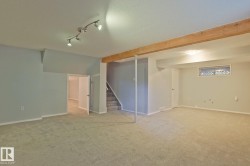 Expansive carpeted area featuring track lighting, a wood beam accent, and a window for natural light - 