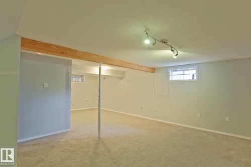 Expansive carpeted area with a light wood-finish beam, track lighting, and multiple windows - 18107 89 Avenue Nw, Edmonton, AB - Indoor