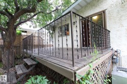 Elevated wood deck with a wrought iron railing, exterior stucco siding, and adjacent mature tree - 