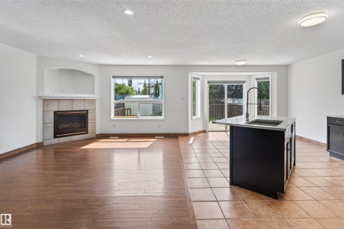 Wood-finish flooring, tile flooring, built-in fireplace with tile surround, kitchen island with integrated sink, sliding glass door - 1707 37A Avenue Nw, Edmonton, AB - Indoor Photo Showing Living Room With Fireplace