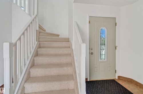 Neutral-toned entry door with decorative glass inserts, carpeted staircase with white balusters, and tile flooring - 1707 37A Avenue Nw, Edmonton, AB - Indoor Photo Showing Other Room