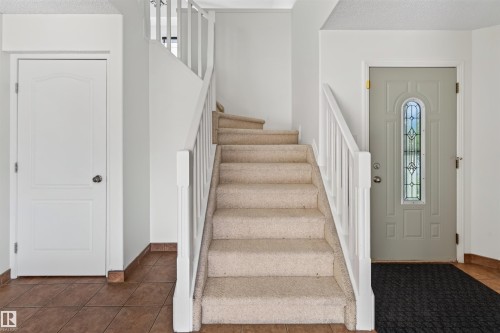 Tiled flooring entry with a carpeted staircase and white balusters - 1707 37A Avenue Nw, Edmonton, AB - Indoor Photo Showing Other Room