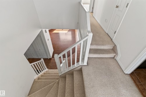 Carpeted staircase with white balusters, leading to a hallway with a paneled door - 1707 37A Avenue Nw, Edmonton, AB - Indoor Photo Showing Other Room