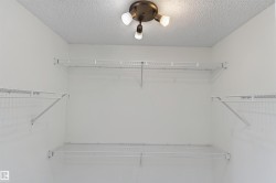 White wire shelving system with multiple tiers, integrated ceiling light fixture, and textured ceiling - 